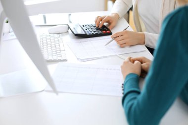 Muhasebeci mali durumu kontrol ediyor ya da vergi formları için hesap makinesi geliri ile sayıyor, eller yakın çekim. İş kadını ofisteki masada iş arkadaşıyla oturuyor ve çalışıyor. Denetim kavramı