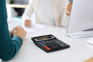 Muhasebeci mali durumu kontrol ediyor ya da vergi formları için hesap makinesi geliri ile sayıyor, eller yakın çekim. İş kadını ofisteki masada iş arkadaşıyla oturuyor ve çalışıyor. Denetim kavramı