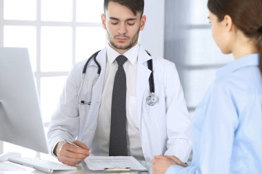 Doktor ve hasta. Tıp bürosunda ya da klinikte cam masada otururken ilaç kayıtlarını dolduran bir doktor. Tıp ve sağlık hizmetleri kavramı