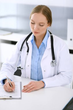 Hastane bürosundaki masada otururken ilaç kayıtlarını dolduran doktor kadın. Hekim kadın iş başında. Tıp ve sağlık alanlarındaki veriler