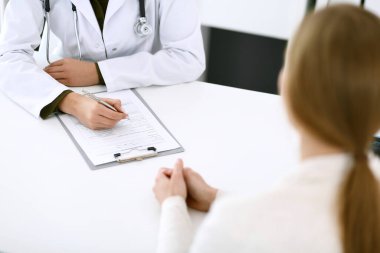 Kadın doktor ve hasta hastane muayenehanesinde oturuyor ve konuşuyor, yakın plan. İlaç kayıtlarını dolduran bir terapist. Tıp ve sağlık hizmetleri kavramı