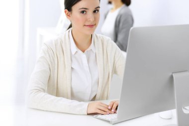 Ofiste bilgisayarla çalışan bir iş kadını, arka planda çalışan bir iş arkadaşı. Masada otururken avukatın ya da muhasebecinin vesikalığı.