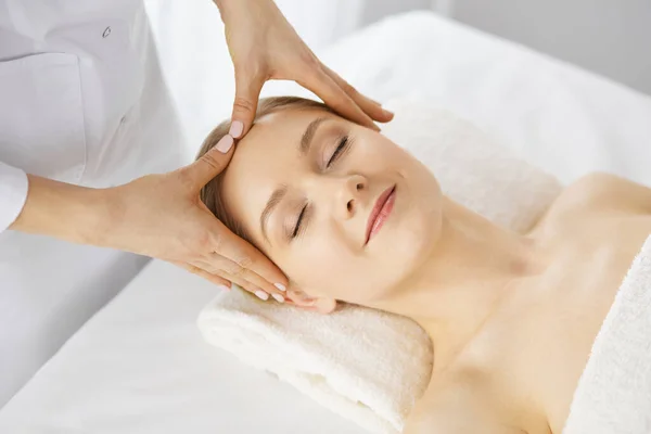 Hermosa mujer caucásica disfrutando de masaje facial con los ojos cerrados en el salón de spa. Tratamiento relajante en medicina y concepto de belleza — Foto de Stock