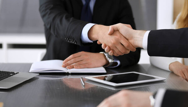 Бизнесмен пожимает руку коллеге или партнеру над стеклянным столом в современном офисе крупным планом. Неизвестные бизнесмены на встрече. Командная работа, партнерство и концепция рукопожатия