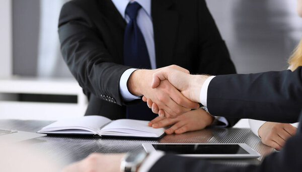 Бизнесмен пожимает руку коллеге или партнеру над стеклянным столом в современном офисе крупным планом. Неизвестные бизнесмены на встрече. Командная работа, партнерство и концепция рукопожатия