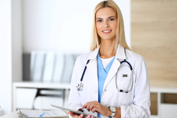 Doctor woman at work in hospital excited and happy of her profession. Blonde physician controls medication history records and exam results while using tablet computer. Medicine and healthcare concept