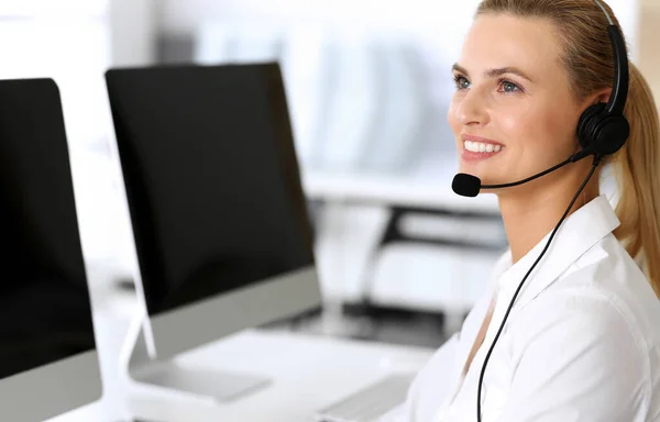 Centro de llamadas. Mujer de negocios feliz y emocionada usando auriculares mientras consulta a clientes en línea. Oficina de servicio al cliente o departamento de telemarketing. Sonriente rubia operadora en el trabajo — Foto de Stock