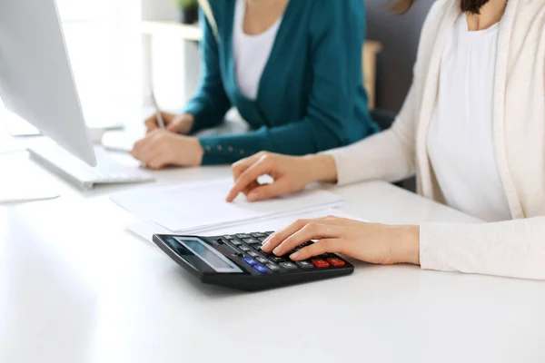 Contabilista verificando ficha financeira ou contando por calculadora de renda para a forma de imposto, mãos close-up. Mulher de negócios sentada e trabalhando com colega na mesa no escritório. Conceito de auditoria — Fotografia de Stock