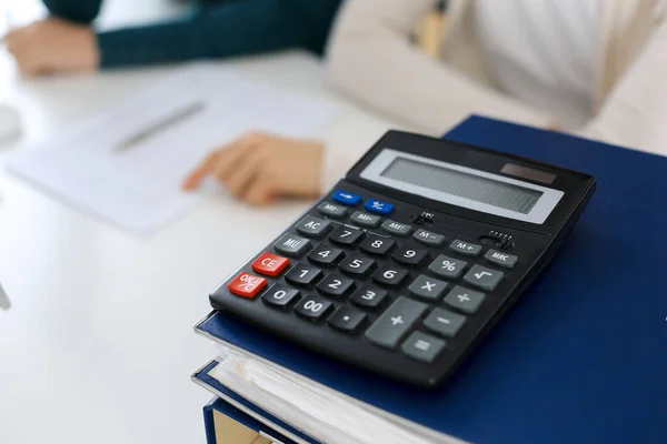 Taschenrechner und Ordner mit Papieren warten darauf, von einer Geschäftsfrau oder Buchhalterin, die am Schreibtisch im Büro arbeitet, verschwommen bearbeitet zu werden. Interne Revision und Steuerkonzept — Stockfoto