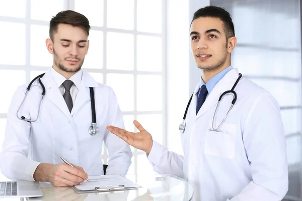 Арабський лікар сидить за скляним столом з колегою по кафедрі медицини або в клініці. Різні лікарі, медицина та медичне обслуговування концепції — стокове фото
