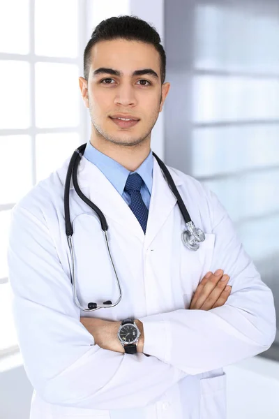 Médico árabe de pie con los brazos cruzados en el consultorio médico o clínica. Concepto de medicina y salud —  Fotos de Stock