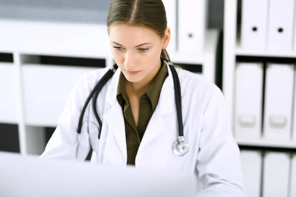 Doktorn skriver på datorn när han sitter vid skrivbordet på sjukhusets kontor. Läkarkvinnan på jobbet. Uppgifter inom medicin och hälsovård — Stockfoto