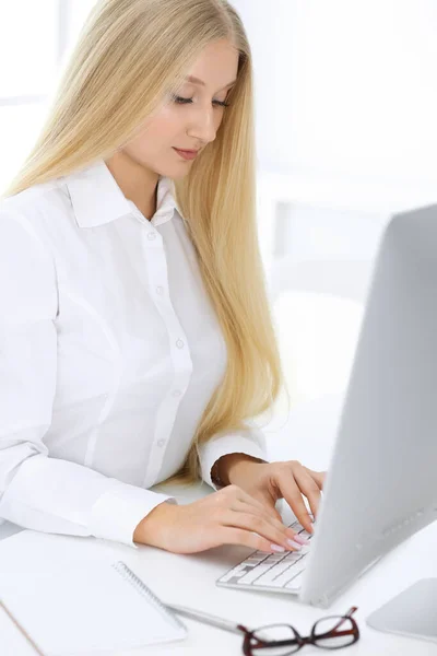 Mujer de negocios rubia sentada y trabajando con computadora en oficina blanca. Estudiante chica estudiando o secretaria haciendo informe. Concepto de éxito —  Fotos de Stock