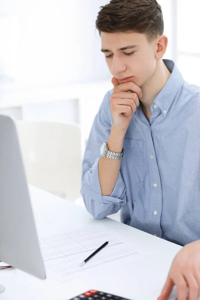 Homem de negócios sentado e trabalhando com computador e calculadora no escritório branco. Estudante a estudar em casa ou jovem contabilista a verificar o equilíbrio. Conceito fiscal, de auditoria e de contabilidade — Fotografia de Stock