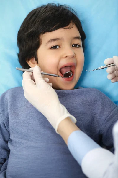 Маленький арабский мальчик сидит в стоматологическом кресле с открытым ртом во время перорального осмотра, пока доктор. Посещение кабинета дантиста. Концепция медицины и стоматологии — стоковое фото