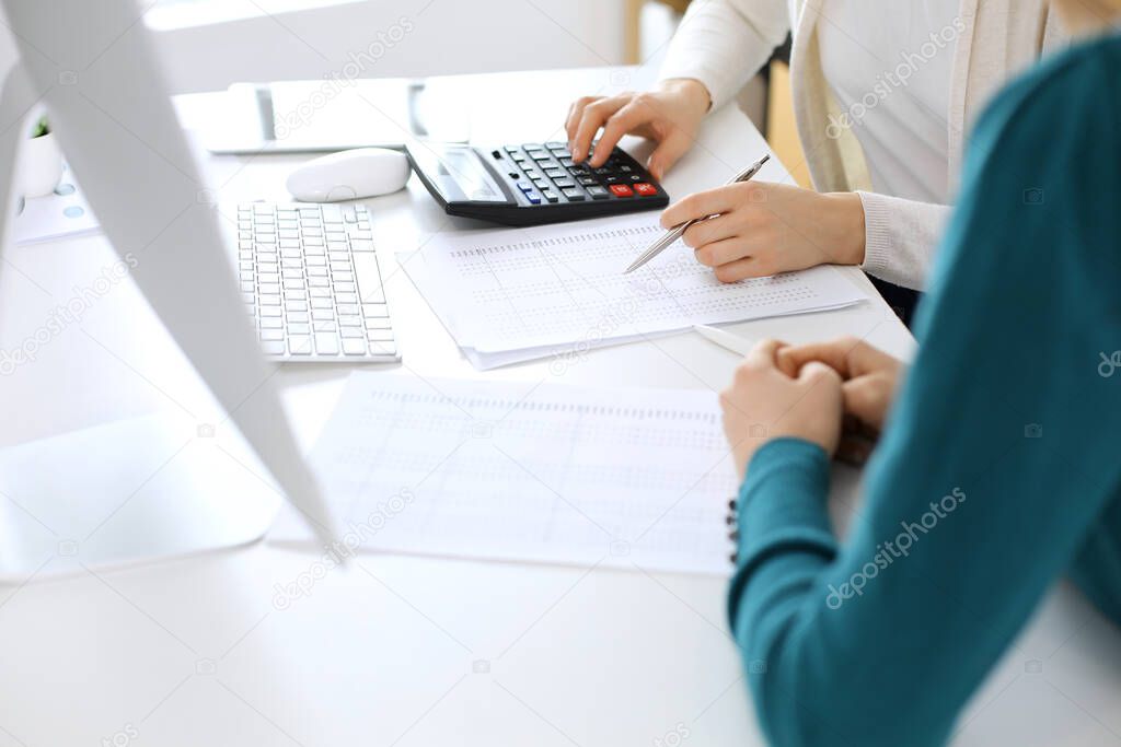 Accountant checking financial statement or counting by calculator income for tax form, hands close-up. Business woman sitting and working with colleague at the desk in office. Audit concept