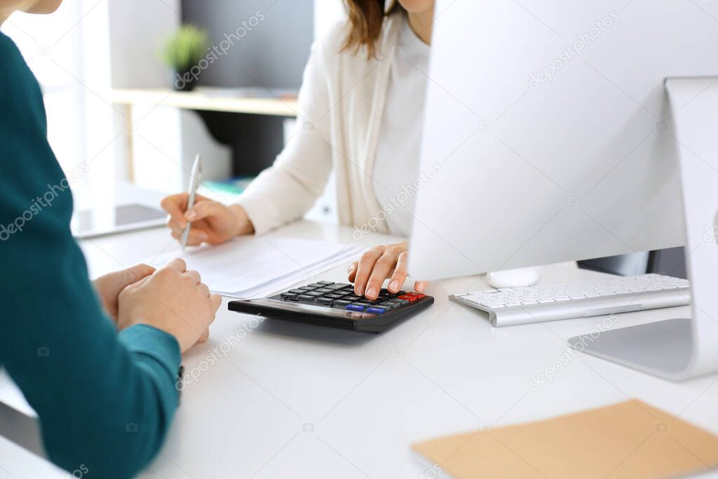 Accountant checking financial statement or counting by calculator income for tax form, hands close-up. Business woman sitting and working with colleague at the desk in office. Audit concept