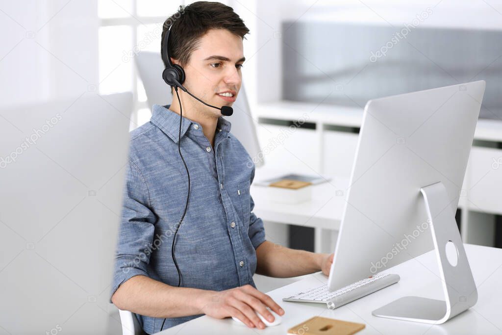 Group of operators at work. Call center. Focus on young man receptionist in headset at customer service. Business concept and casual clothing style