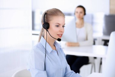 Merkezi ara. İnternette müşterilere danışmak için bilgisayar ve kulaklık kullanan güzel sarışın kadın. Müşteri hizmetleri işgali olarak çalışan bir grup operatör. İş adamları konsepti