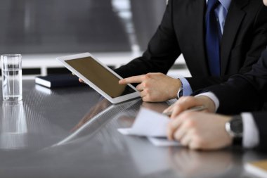 İşadamı tablet bilgisayar kullanıyor ve iş arkadaşı ya da ortağıyla modern ofiste cam masada çalışıyor. Yakın plan. Toplantıda bilinmeyen iş adamları var. Takım çalışması ve ortaklık kavramı