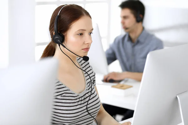 Group of operators at work. Call center. Focus on beautiful woman receptionist in headset at customer service. Business concept and casual striped clothing style — Stock Photo, Image