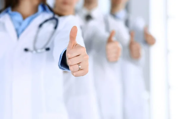 Bir grup modern doktor hastane ofisinde baş parmakları havada bir takım gibi duruyorlar. Doktorlar hastaları muayene etmeye ve yardım etmeye hazır. Tıbbi yardım, sağlık sigortası, en iyi hastalık tedavisi ve ilaç
