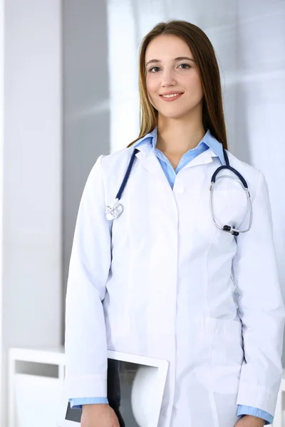 Medico donna felice e allegro mentre in piedi in ufficio ospedaliero in evidenza sfondo. Medicina e concetto di assistenza sanitaria — Foto Stock
