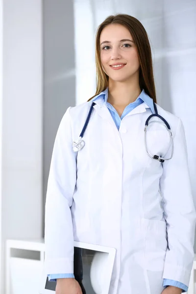 Doctora mujer feliz y alegre, mientras que de pie en la oficina del hospital en el fondo de luz. Concepto de medicina y salud — Foto de Stock