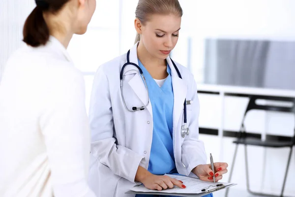 Dokter en patiënt tijdens overleg. Artsen op het werk vullen medicatie geschiedenis record tijdens het zitten in noodgevallen ziekenhuis, portret schieten. Begrip "geneeskunde en gezondheidszorg" — Stockfoto