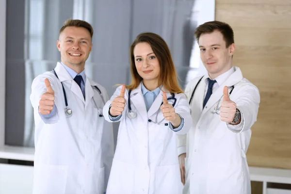 Bir grup modern doktor hastane ofisinde baş parmakları havada ya da OK imzalı bir takım gibi duruyorlar. Doktorlar hastaları muayene etmeye ve yardım etmeye hazır. Tıbbi yardım, sağlık sigortası, en iyi tedavi ve