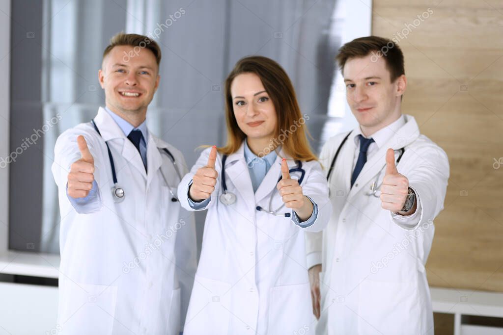 Group of modern doctors standing as a team with thumbs up or Ok sign in hospital office. Physicians ready to examine and help patients. Medical help, insurance in health care, best treatment and