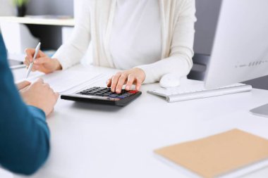 Mali durumu kontrol eden ya da vergi formları için hesap makinesinin geliri ile sayan, elleri yakın çekim. İş kadını ofisteki masada iş arkadaşıyla oturuyor ve çalışıyor. Vergi ve Denetim kavramı