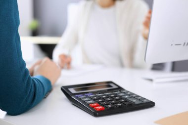 Mali durumu kontrol eden ya da vergi formları için hesap makinesinin geliri ile sayan, elleri yakın çekim. İş kadını ofisteki masada iş arkadaşıyla oturuyor ve çalışıyor. Vergi ve Denetim kavramı