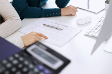 Mali durumu kontrol eden ya da vergi formları için hesap makinesinin geliri ile sayan, elleri yakın çekim. İş kadını ofisteki masada iş arkadaşıyla oturuyor ve çalışıyor. Vergi ve Denetim kavramı