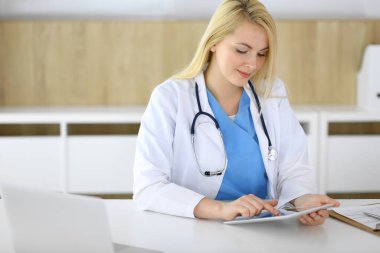 Hastane ya da klinikte tablet kullanan kadın doktor. Sarışın terapist neşeyle gülümsüyor. Tıp ve sağlık konsepti verileri