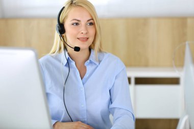 Merkezi ara. Müşteri hizmetleri ofisinde kulaklık takan sarışın bir iş kadını. Telesellerin iş ya da ev işgali kavramı