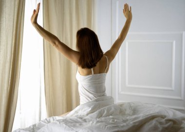 Bir kadın uyandıktan sonra yatakta geriniyor, geriye bakıyor, bir güne mutlu ve rahat giriyor iyi bir gece uykusundan sonra. Esmer için günaydın ve yeni bir gün. Hafta sonu kavramı, tatiller