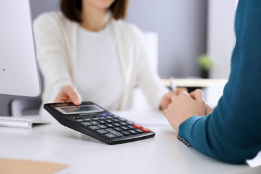 Mali durumu kontrol eden ya da vergi formları için hesap makinesinin geliri ile sayan, elleri yakın çekim. İş kadını, iş yerinde iş arkadaşıyla birlikte mavi tonda oturuyor. Vergi ve