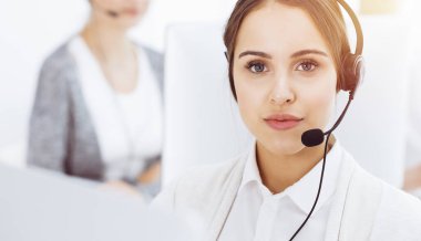 Güneşli ofiste çağrı merkezi. Çeşitli operatörler iş başında. Telepazarlama servisinin müşterileriyle iletişim kuran kulaklıklı güzel bir kadın. İş konsepti