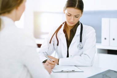Kadın-doktor ve hasta güneşli hastane ofisinde oturup konuşuyorlar. Yeşil renkli bluz terapiste yakışır. Tıp konsepti