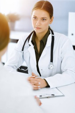 Kadın-doktor ve hasta güneşli hastane ofisinde oturup konuşuyorlar. Yeşil renkli bluz terapiste yakışır. Tıp konsepti