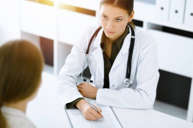 Kadın-doktor ve hasta güneşli hastane ofisinde oturup konuşuyorlar. Yeşil renkli bluz terapiste yakışır. Tıp konsepti
