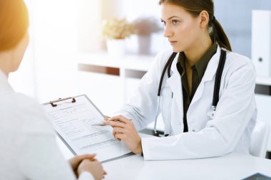 Kadın-doktor ve hasta güneşli hastane ofisinde oturup konuşuyorlar. Yeşil renkli bluz terapiste yakışır. Tıp konsepti