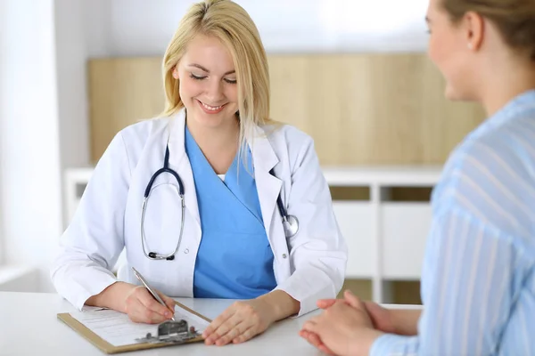 Mujer médico y paciente sentado y hablando en el examen médico en el hospital o clínica. Terapeuta rubia sonriendo alegremente. Concepto de medicina y salud — Foto de Stock