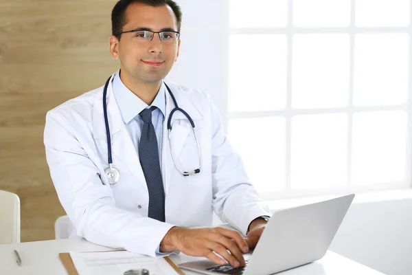 Medico uomo digitando al computer portatile mentre seduto alla scrivania al suo posto di lavoro. Servizio medico perfetto in clinica. Dati in medicina e sanità — Foto Stock