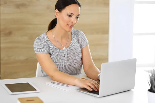 현대인 사무실의 책상에 앉아서 노트북 컴퓨터로 일하는 쾌활하게 웃는 사업가. 중년의 여성 변호사나 감사관 이 일하고 있습니다. 사업가들의 개념 — 스톡 사진