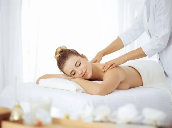 Young and blonde woman enjoying massage of back in spa salon. Beauty concept — Stock Photo, Image