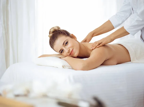 Young and blonde woman enjoying massage of back in spa salon. Beauty concept — Stock Photo, Image