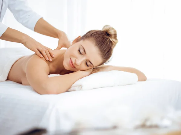 Young and blonde woman enjoying massage of back in spa salon. Beauty concept — Stock Photo, Image