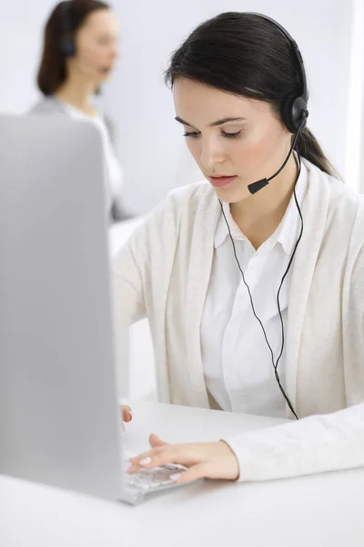 Centro de llamadas. Mujer vestida casual sentada en auriculares en la oficina de servicio al cliente. Grupo de operadores en el trabajo. Concepto empresarial —  Fotos de Stock